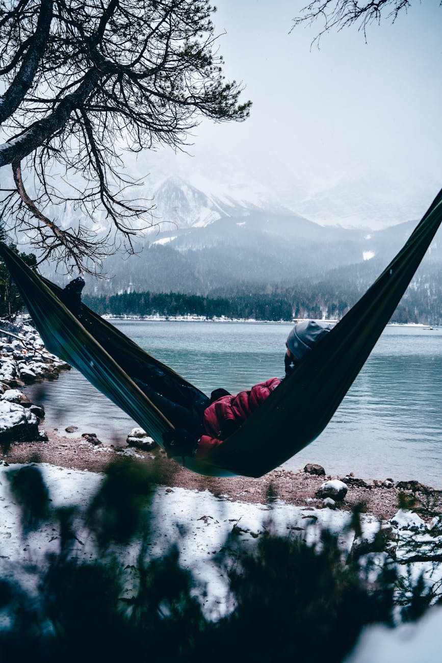 a person relaxes in a hammock by a snowy alpine lake with mountains in bavaria