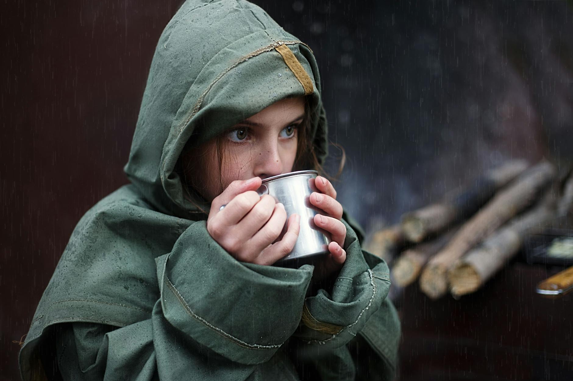 young girl in raincoat sipping warm beverage on a rainy day in the forest