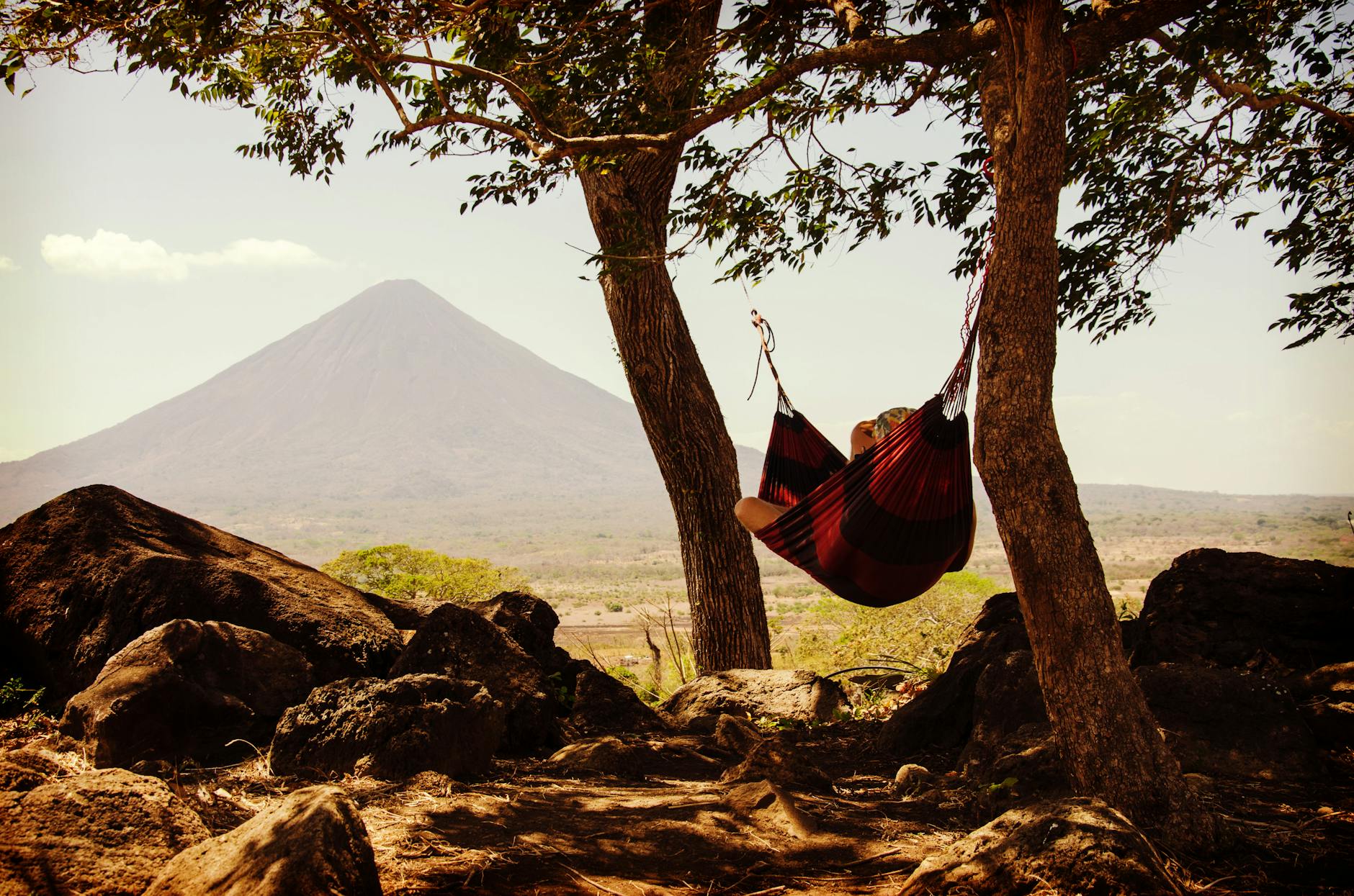 person relaxing in a hammock between trees with a volcano in the background capturing tranquility and nature