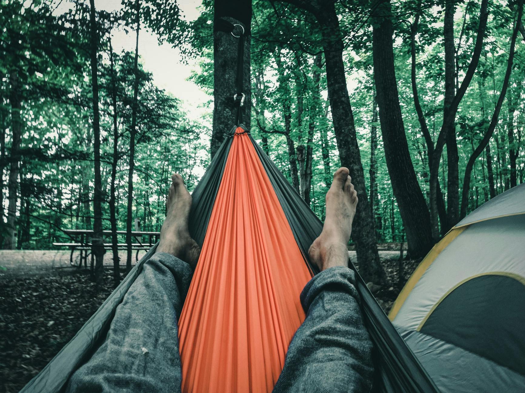 feet up in hammock at forest campsite with view of trees and tent