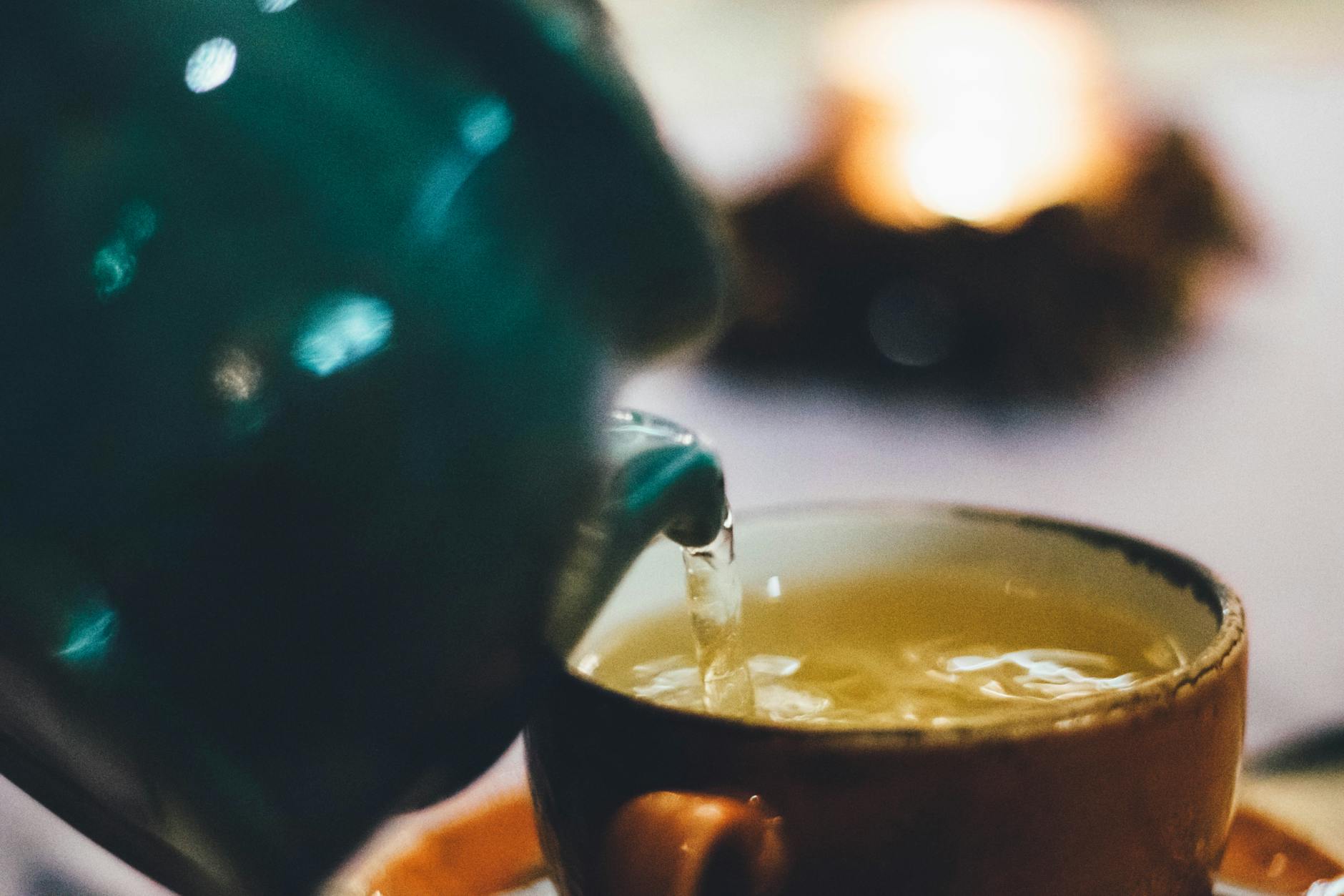 personne versant du liquide dans une tasse en ceramique brune