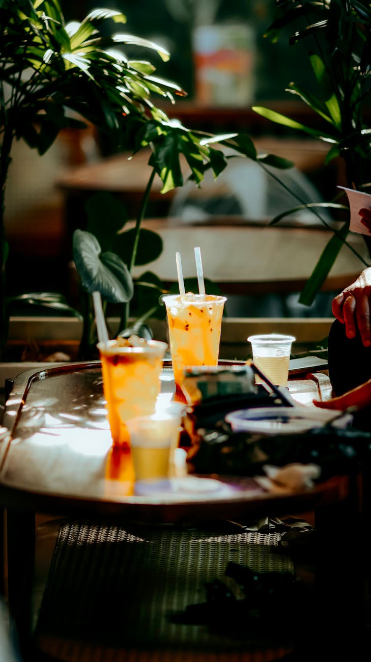 des verres de bubble tea glaces avec des pailles entoures de plantes luxuriantes sur une table de cafe ensoleillee en terrasse