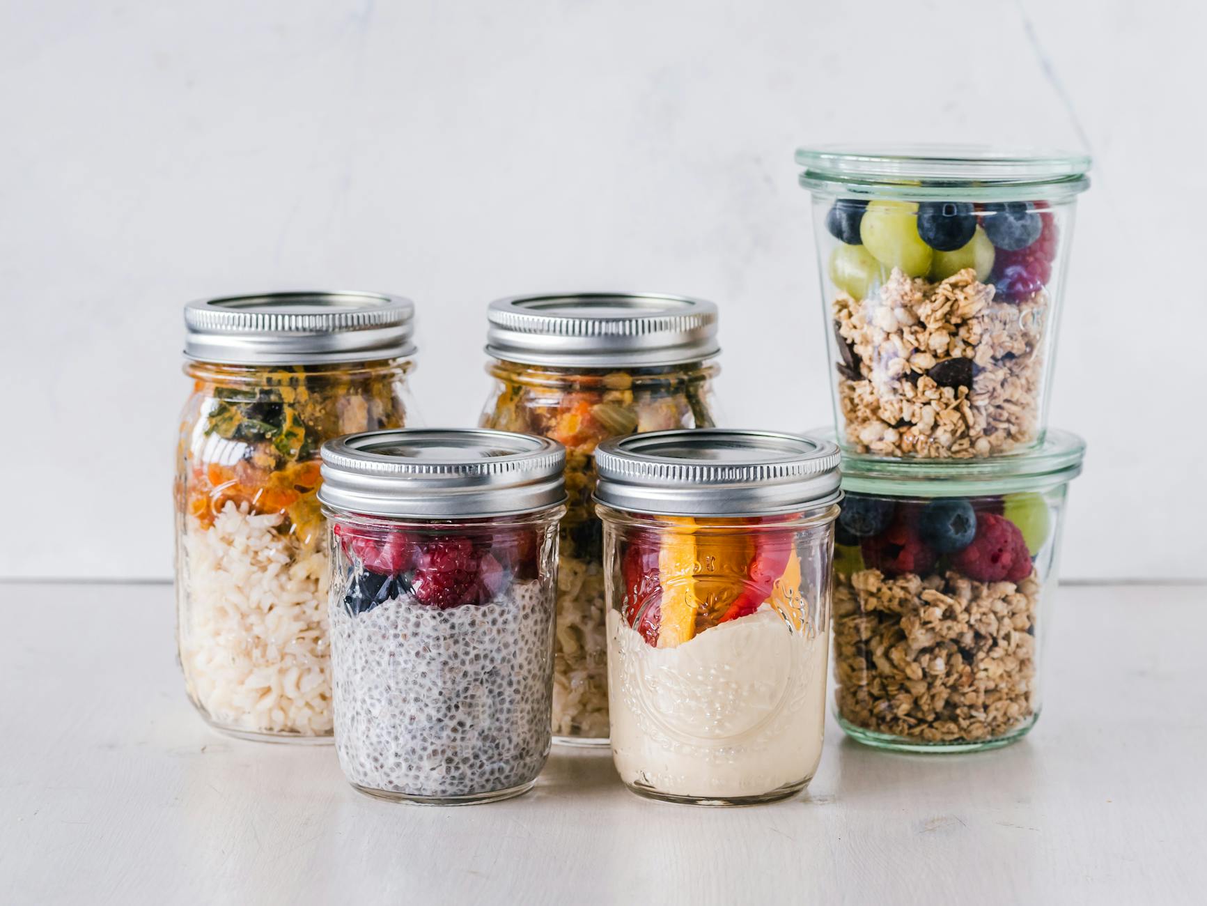 six cereales aux fruits dans des bocaux mason en verre transparent sur surface blanche