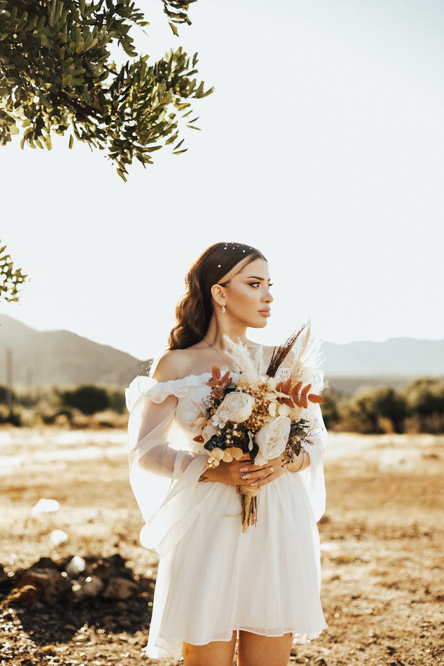 une mariee en robe blanche tenant un bouquet de fleurs dans un paysage naturel et ensoleille