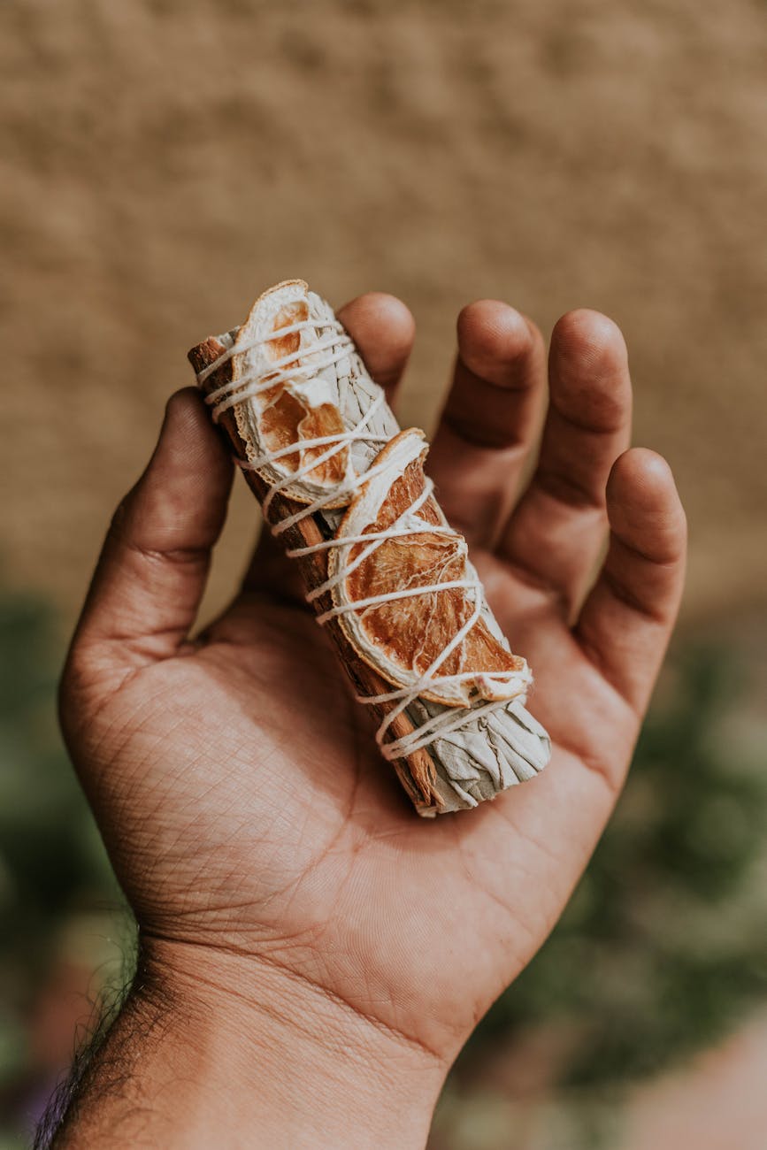 Une main tient délicatement un bouquet de sauge séchée et de tranches dorange, enveloppé de ficelle