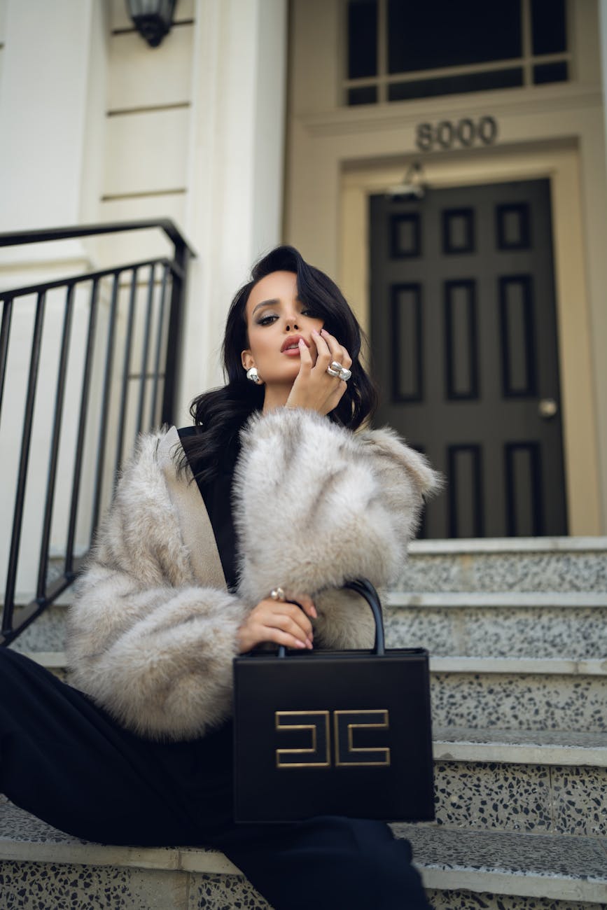 une femme a la mode en manteau de fourrure pose avec un sac a main de luxe sur les marches de la ville