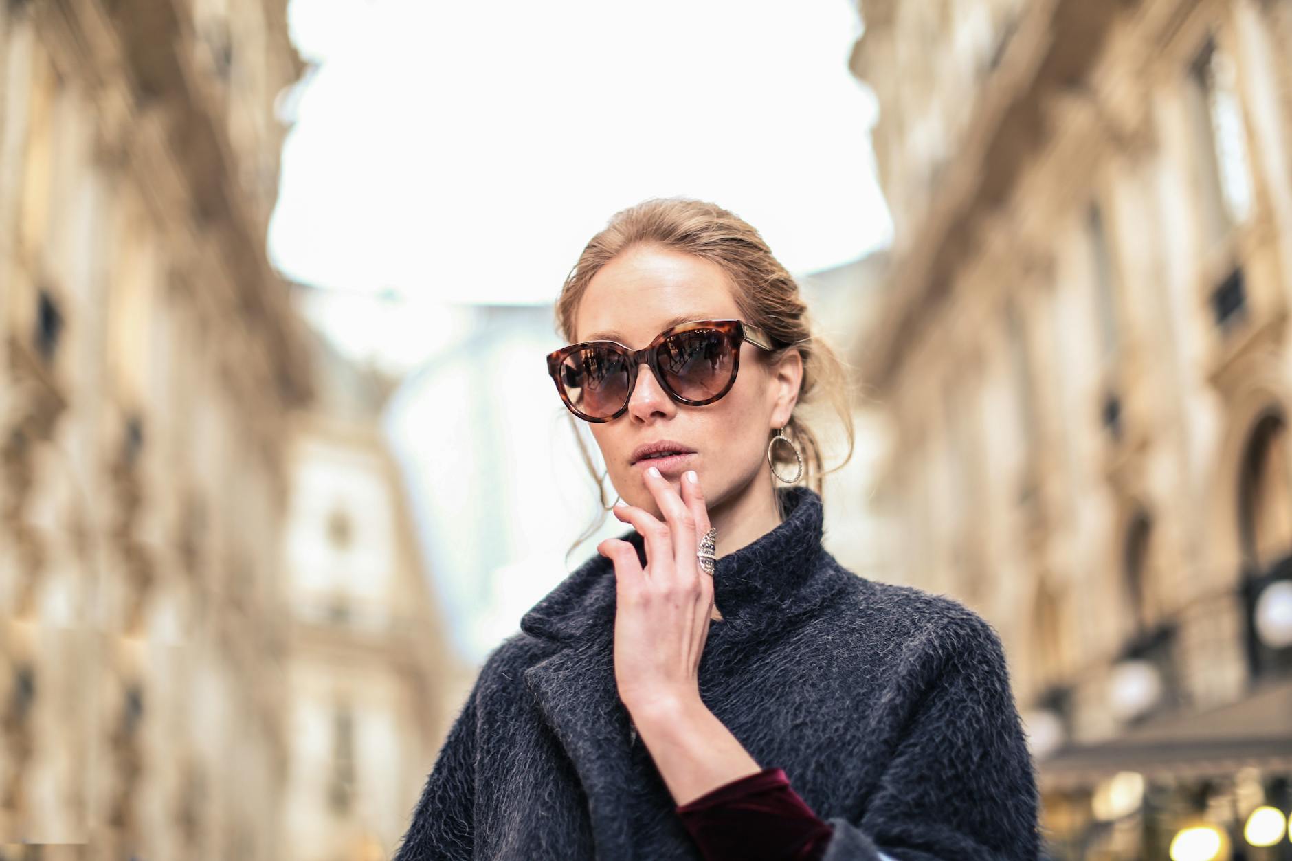 femme portant un manteau noir et des lunettes de soleil encadrees marron