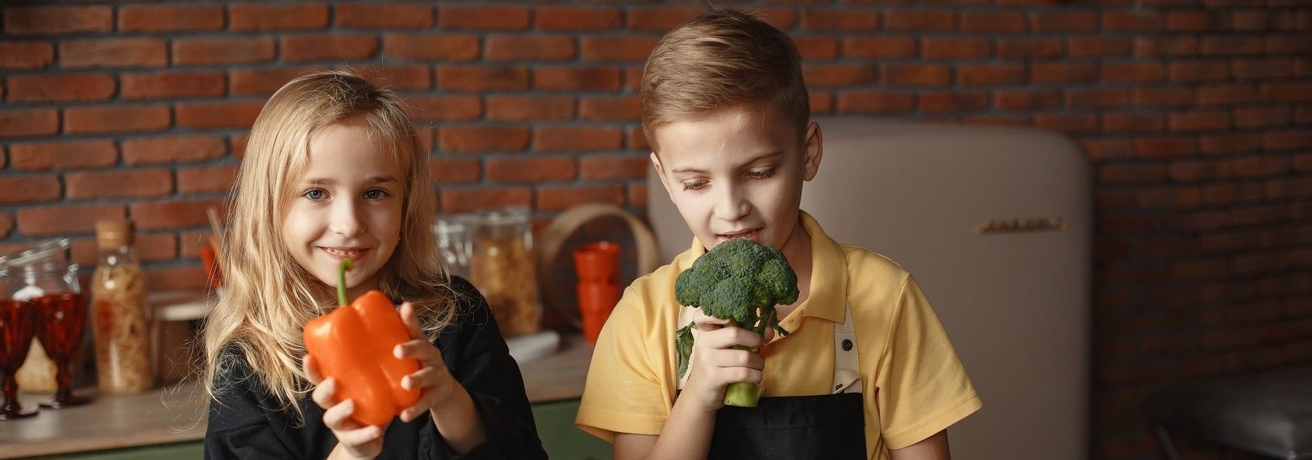 deux enfants joyeux dans une cuisine tenant des legumes frais promouvant un mode de vie sain