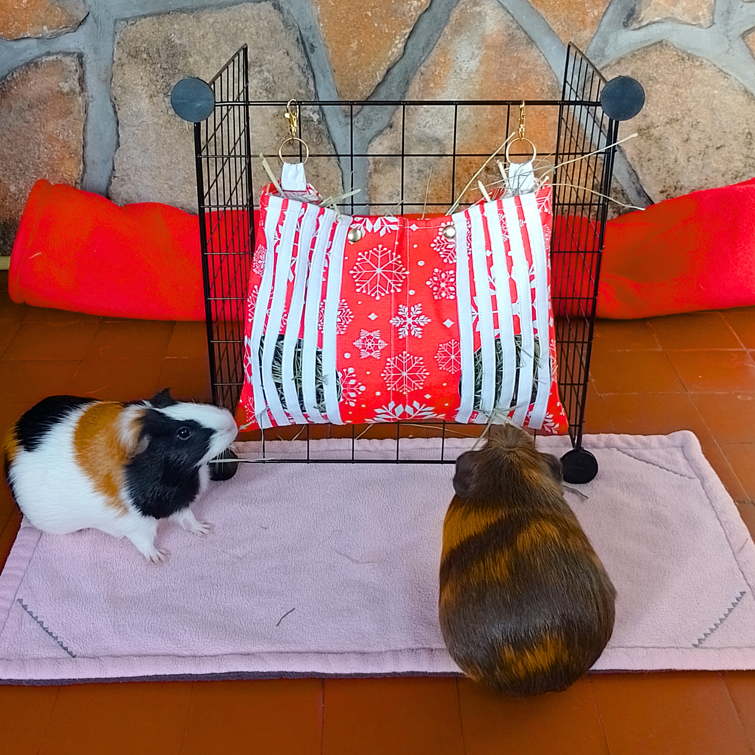 Sac-à-foin-personnalisable-pour-lapin-en-tissu-coton-rouge-à-flocons-accroché-à-une-grille-avec-attaches-dorées