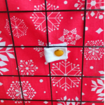 Sac-à-foin-personnalisable-pour-lapin-en-tissu-coton-rouge-à-flocons-accroché-à-une-grille-avec-attaches-dorées-2
