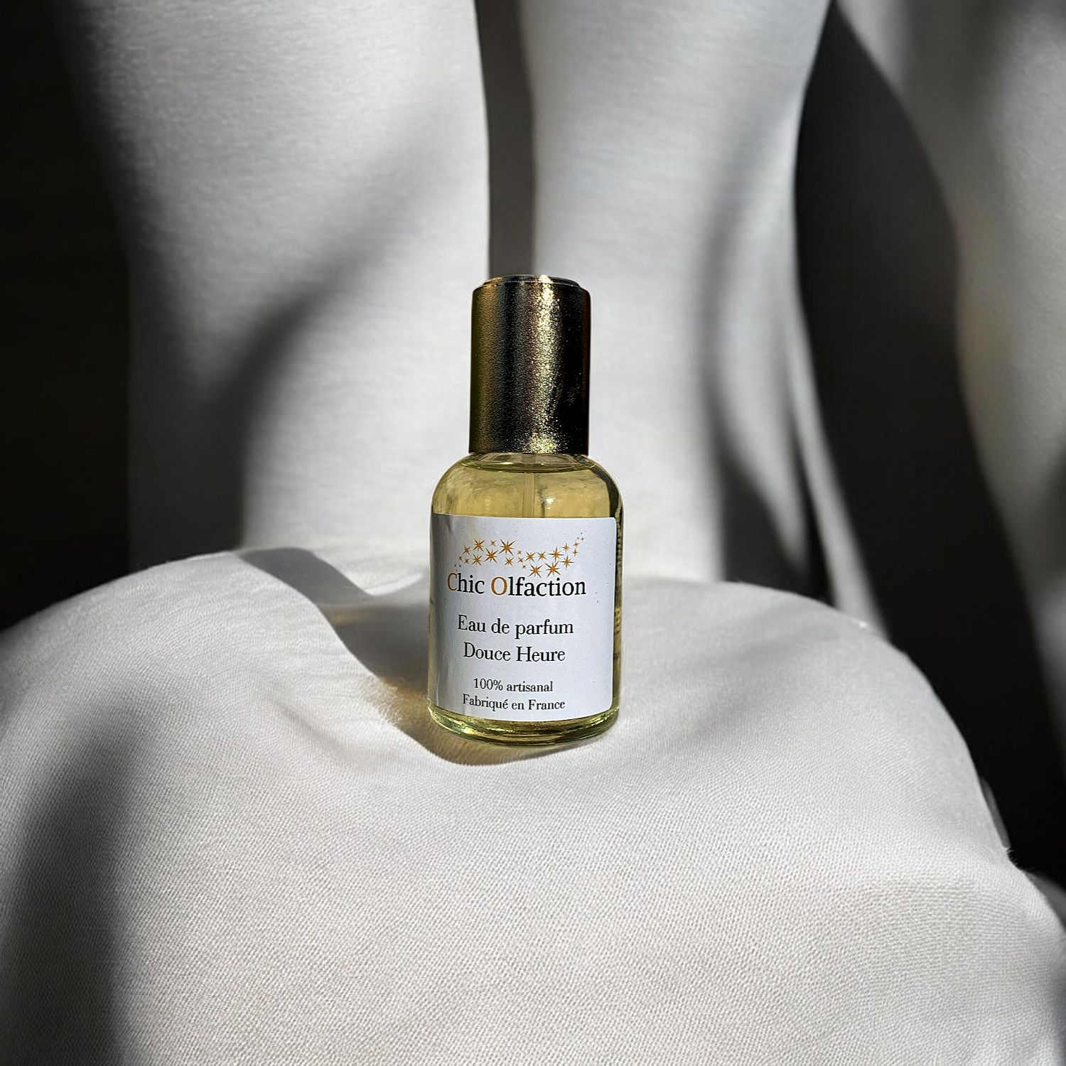 flacon deau de parfum de la marque chic olfaction portant le nom de douce heure posé sur un coussin couleur chair devant un dos nu