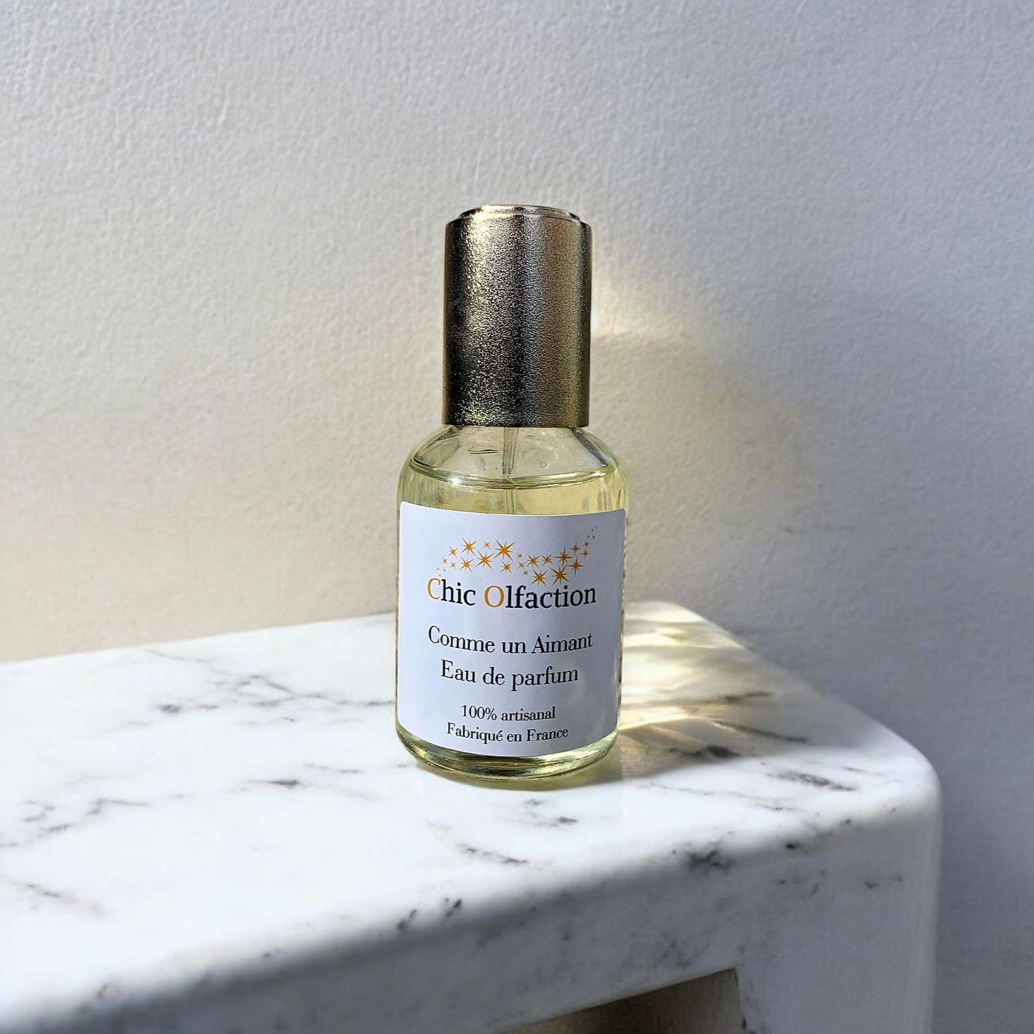 flacon de 50 ml deau de parfum de la marque chic olfaction portant le nom de comme un aimant posé sur une console en marbre
