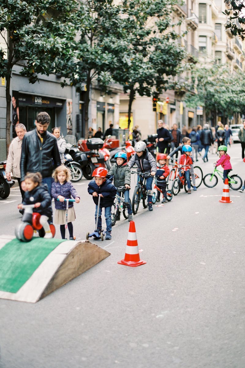 kids participating in a street event riding bicycles and scooters among traffic cones