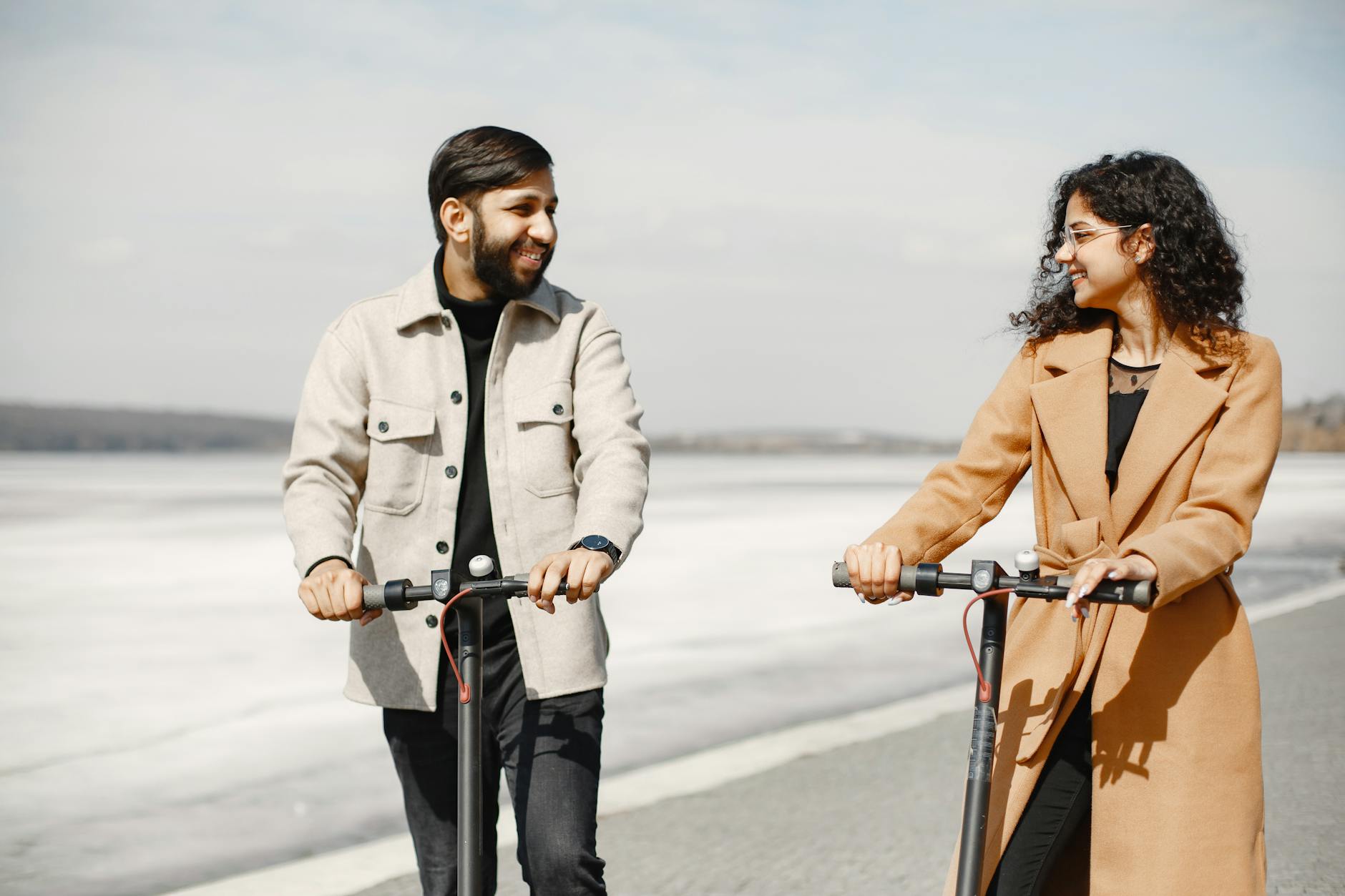 smiling couple riding electric scooters on a sunny seaside day