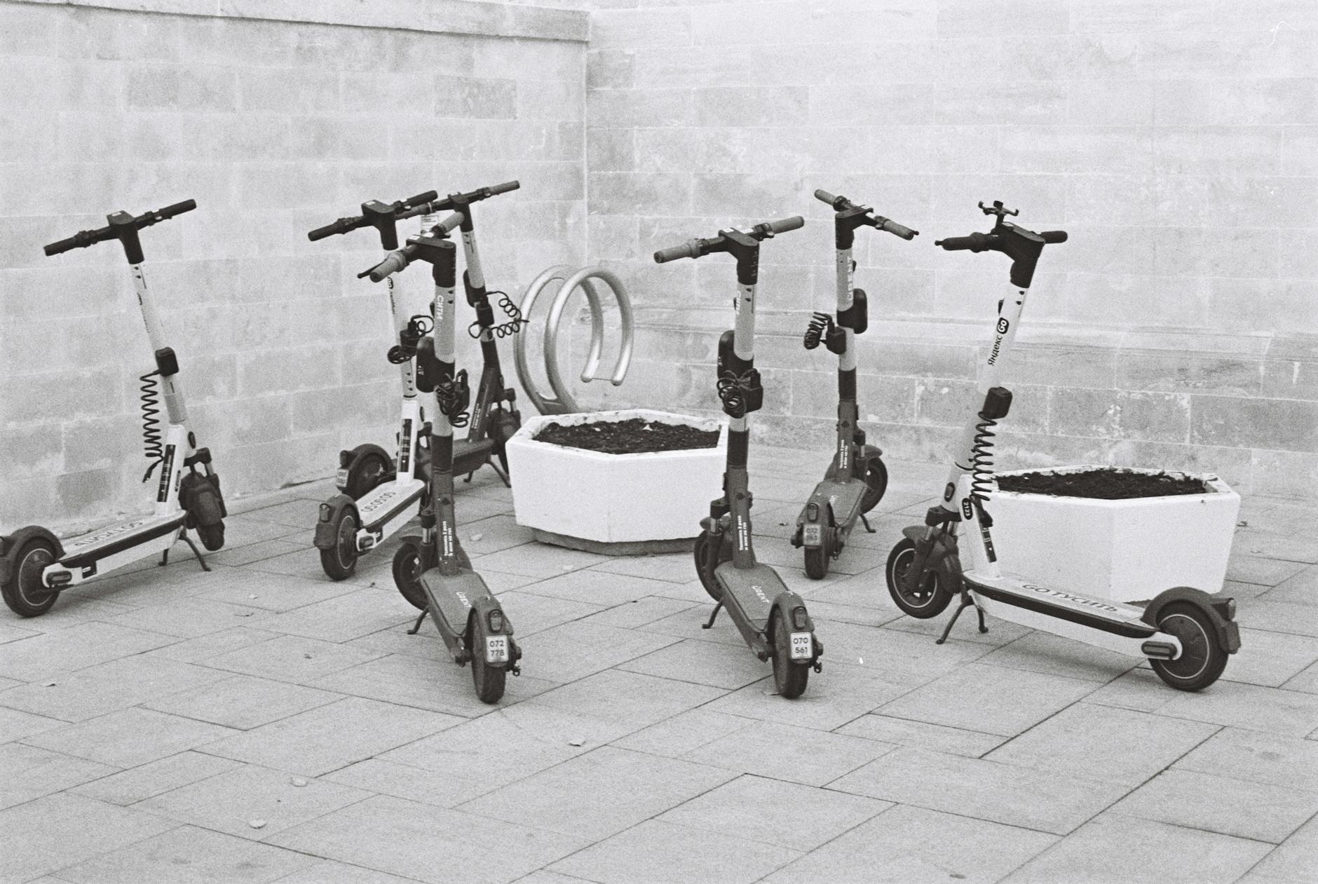 black and white photo of several electric scooters parked beside concrete planters