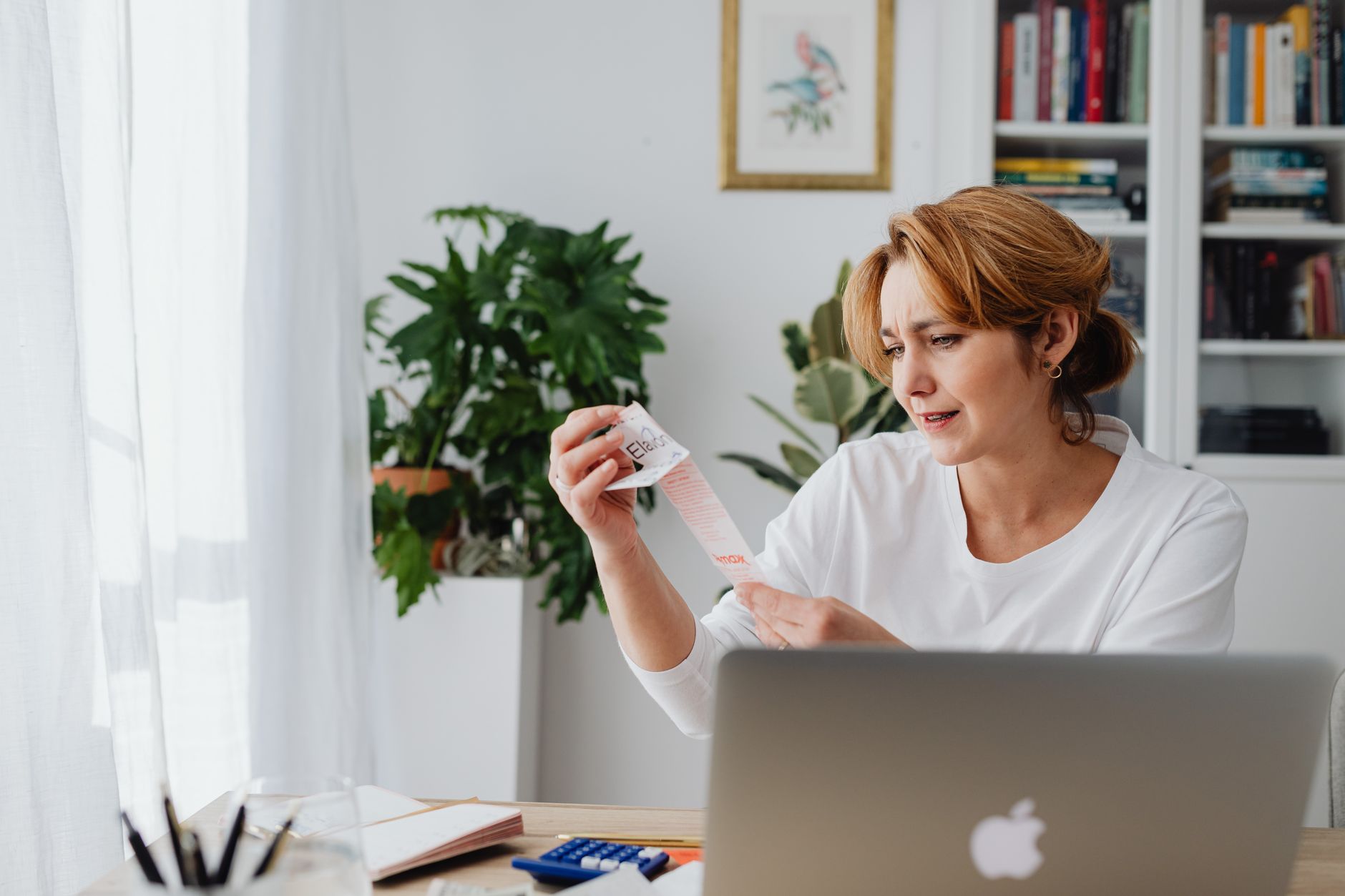 Une femme examine un ticket de caisse devant son ordinateur et une calculatrice