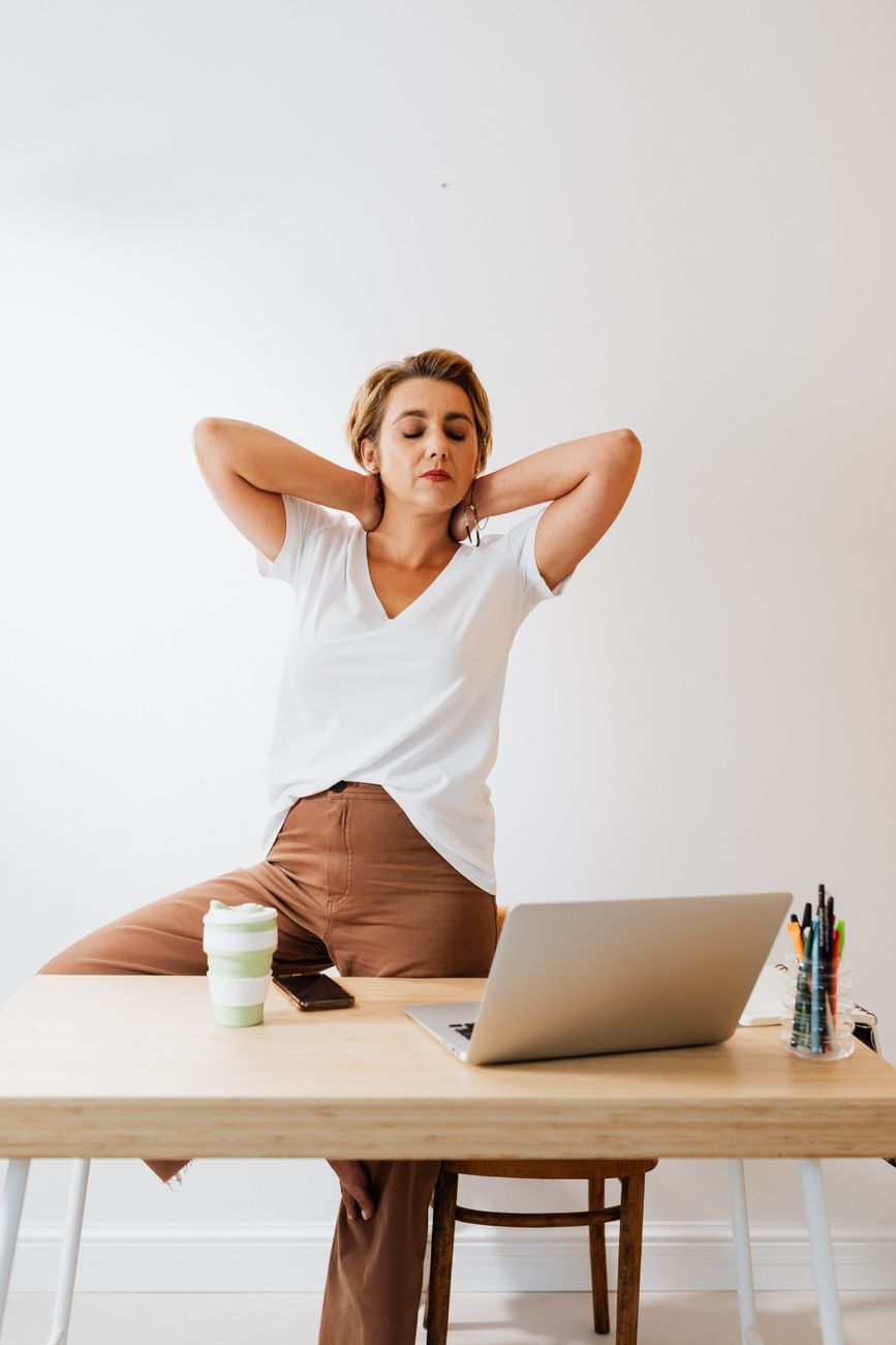 Une femme s’étire derrière son bureau et son ordinateur portable