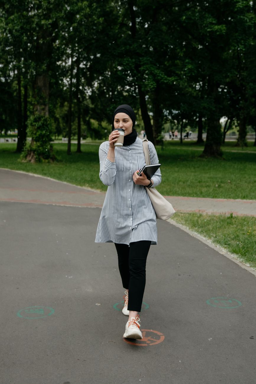 Une femme marche dans un parc avec un carnet et une tasse