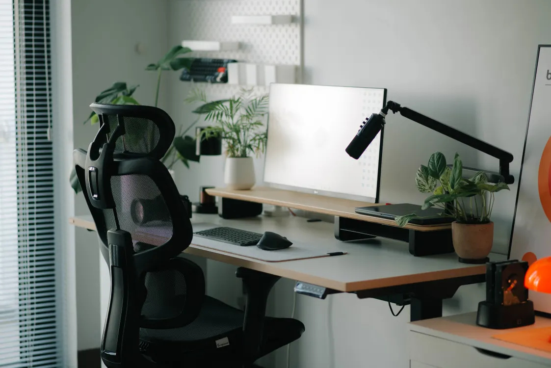 Chaise de bureau noire à dossier en résille devant un bureau avec écran et clavier séparé