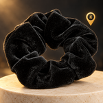 Zwarte fluwelen scrunchie met tracker op een lichte sokkel met gouden verlichting