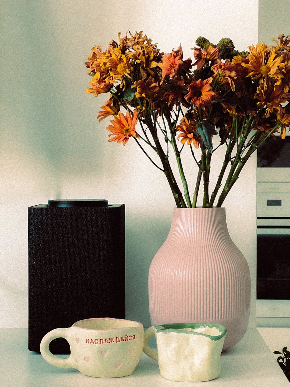 aesthetic indoor setup featuring autumn flowers in a pink vase alongside an air purifier and decorative mugs