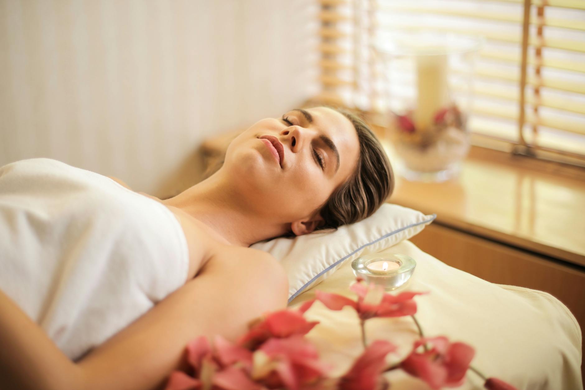 femme enveloppee dans une serviette blanche allongee sur le lit avec les yeux fermes