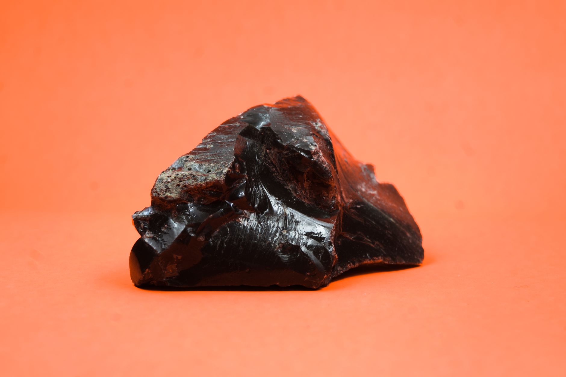 une roche d obsidienne noire aux contours nets se detachant sur un fond orange et mettant en valeur sa texture brillante