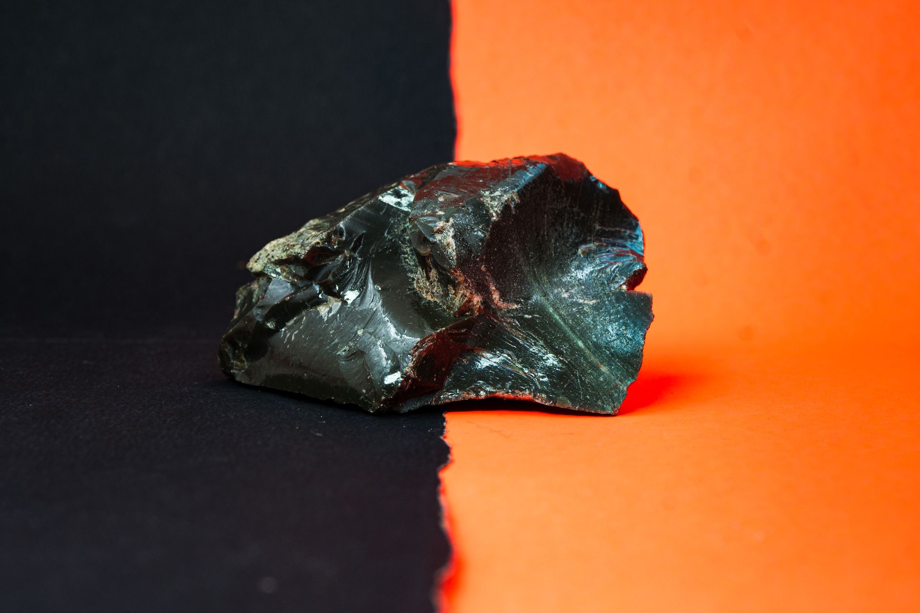 une pierre d obsidienne brute presentee sur un fond noir et orange saisissant mettant en valeur sa texture et son eclat