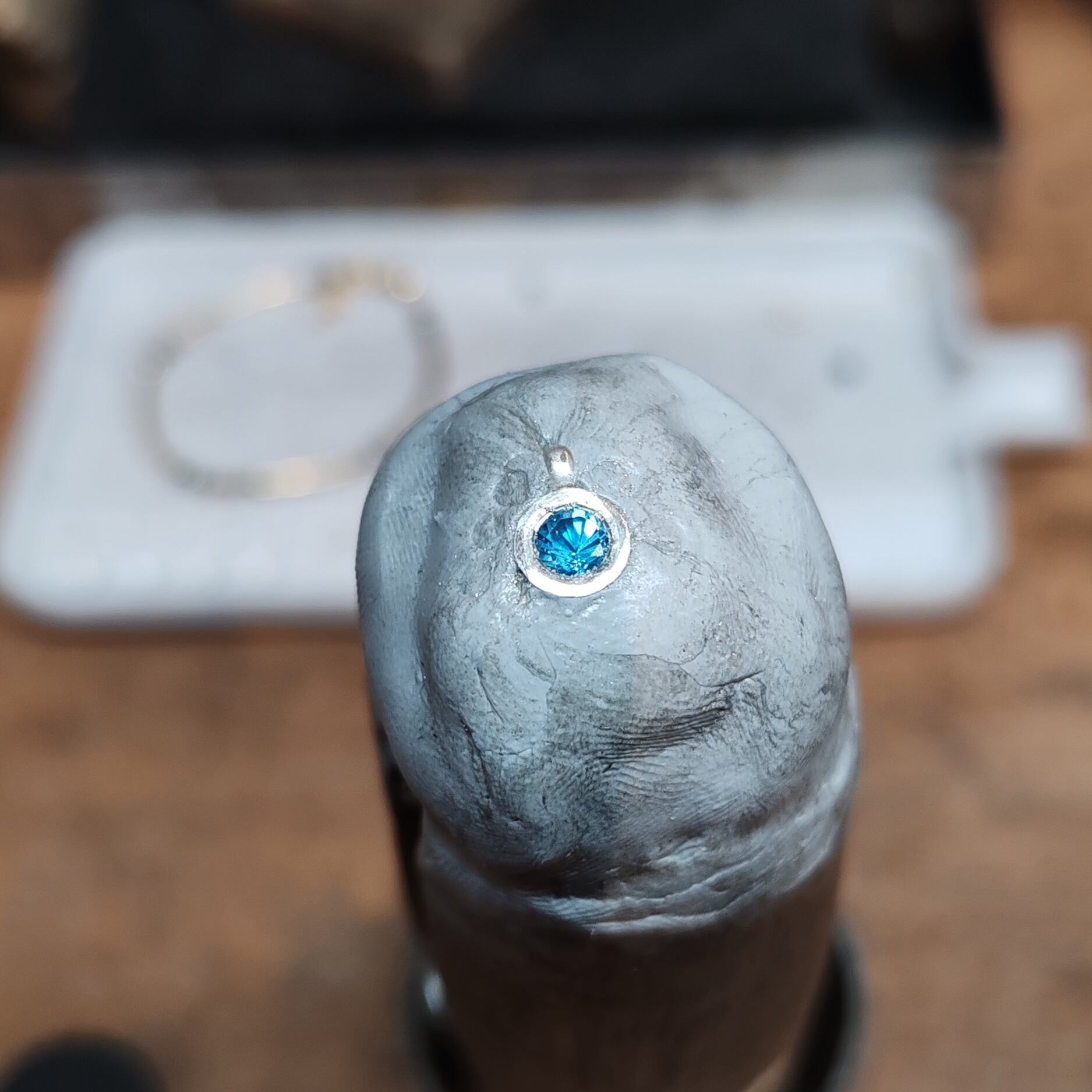 Détail macro du sertissage artisanal dun pendentif en argent 925 avec topaze bleue par un bijoutier. Gros plan sur la pierre fine et le serti clos en cours de fabrication à Valbonne