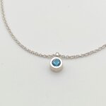 Vue rapprochée (gros plan) du pendentif en argent massif 925 orné dune topaze bleue fine à facettes. Serti clos artisanal, sur chaîne maille vénitienne. Photographie de détail sur fond blanc