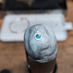 Détail macro du sertissage artisanal dun pendentif en argent 925 avec topaze bleue par un bijoutier. Gros plan sur la pierre fine et le serti clos en cours de fabrication à Valbonne