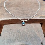 Collier pendentif en argent 925 avec topaze fine bleue et chaîne maille vénitienne posé sur létabli en bois dun bijoutier. Bijou artisanal moderne et raffiné en argent massif