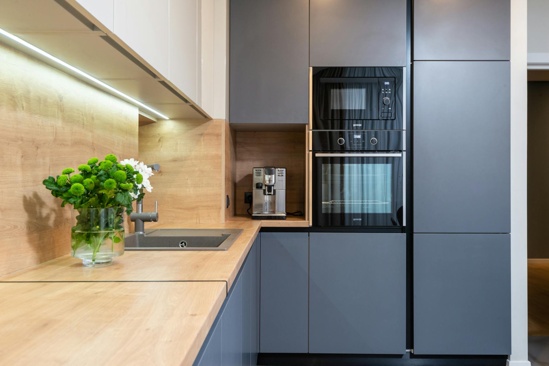 creative design of kitchen with built in oven against coffee machine and flowers in vase on table in house