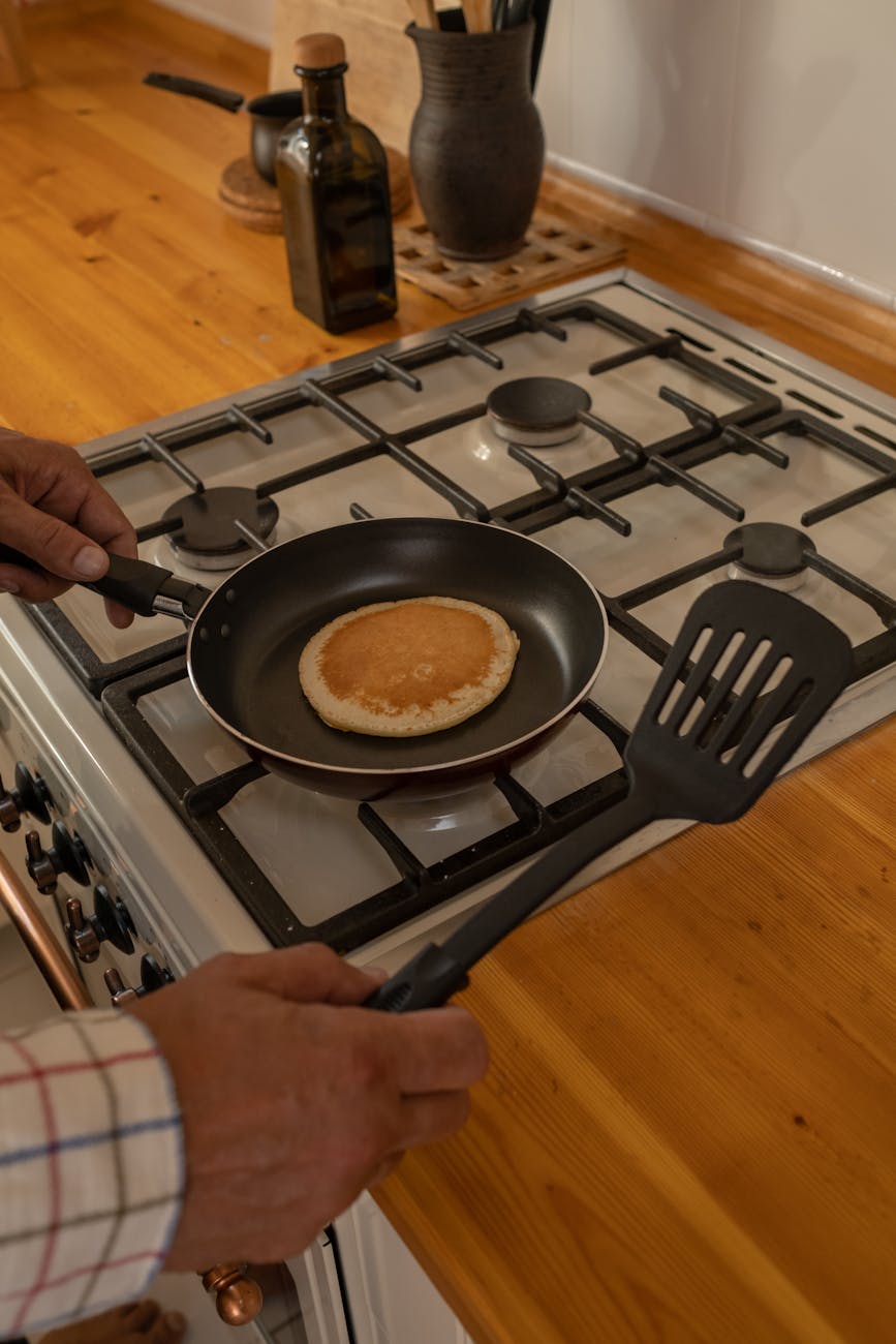 a person cooking pancakes on a gas stove in a cozy kitchen setting