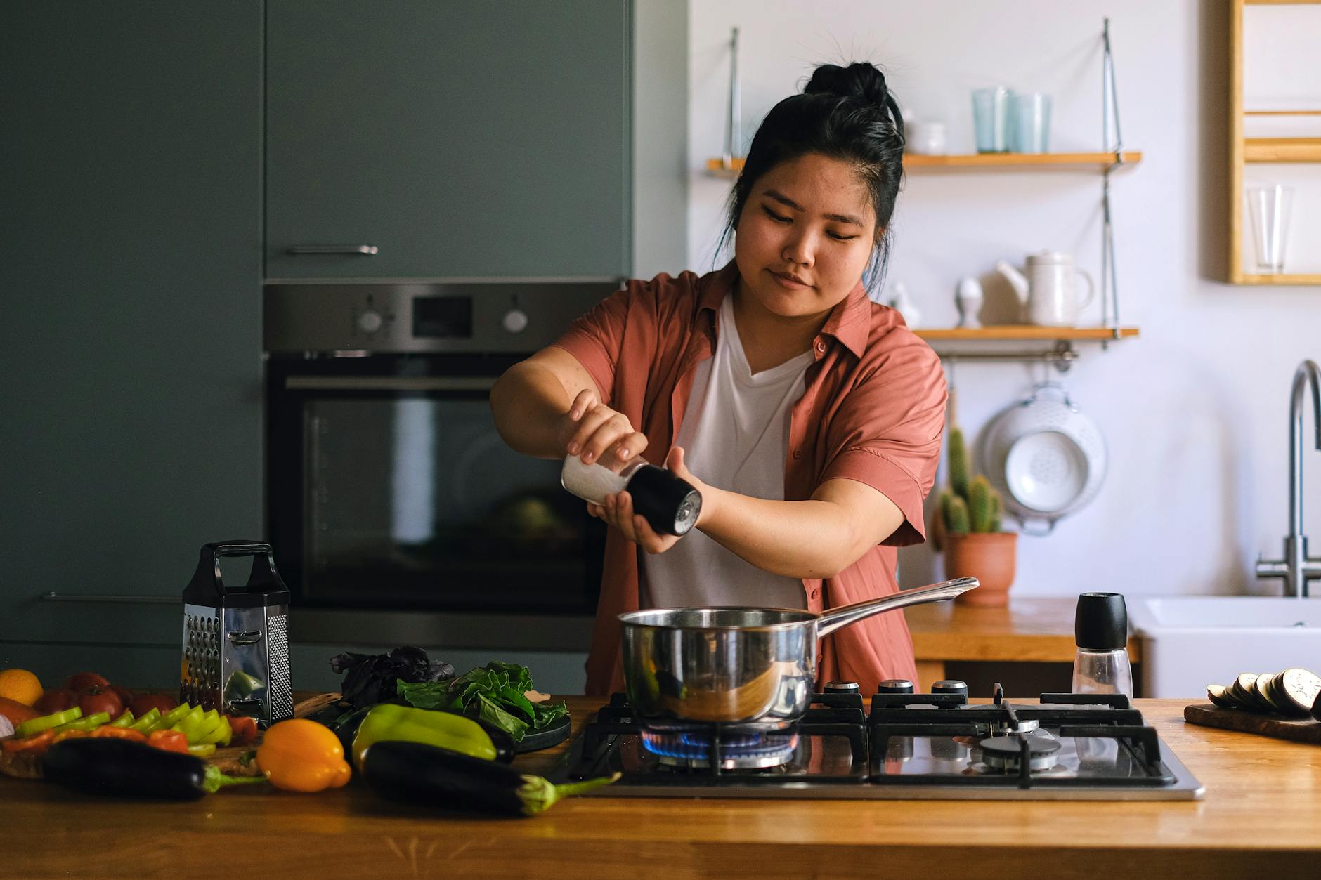 a home cook seasoning a dish on a stove surrounded by fresh vegetables in a modern kitchen