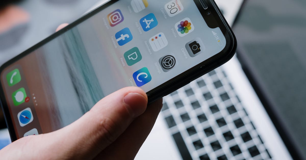 person holding a smartphone in front of a laptop showcasing various app icons highlighting digital connectivity