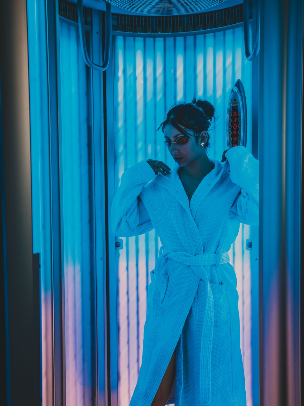 femme portant un peignoir et des lunettes a l interieur d une cabine de bronzage dans un spa de beaute