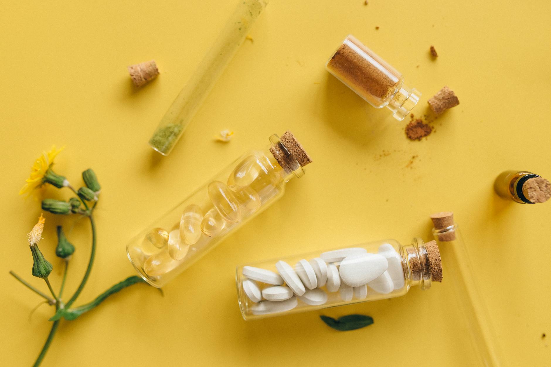 top view of medicinal herbs pills and powders in bottles against a vibrant yellow backdrop