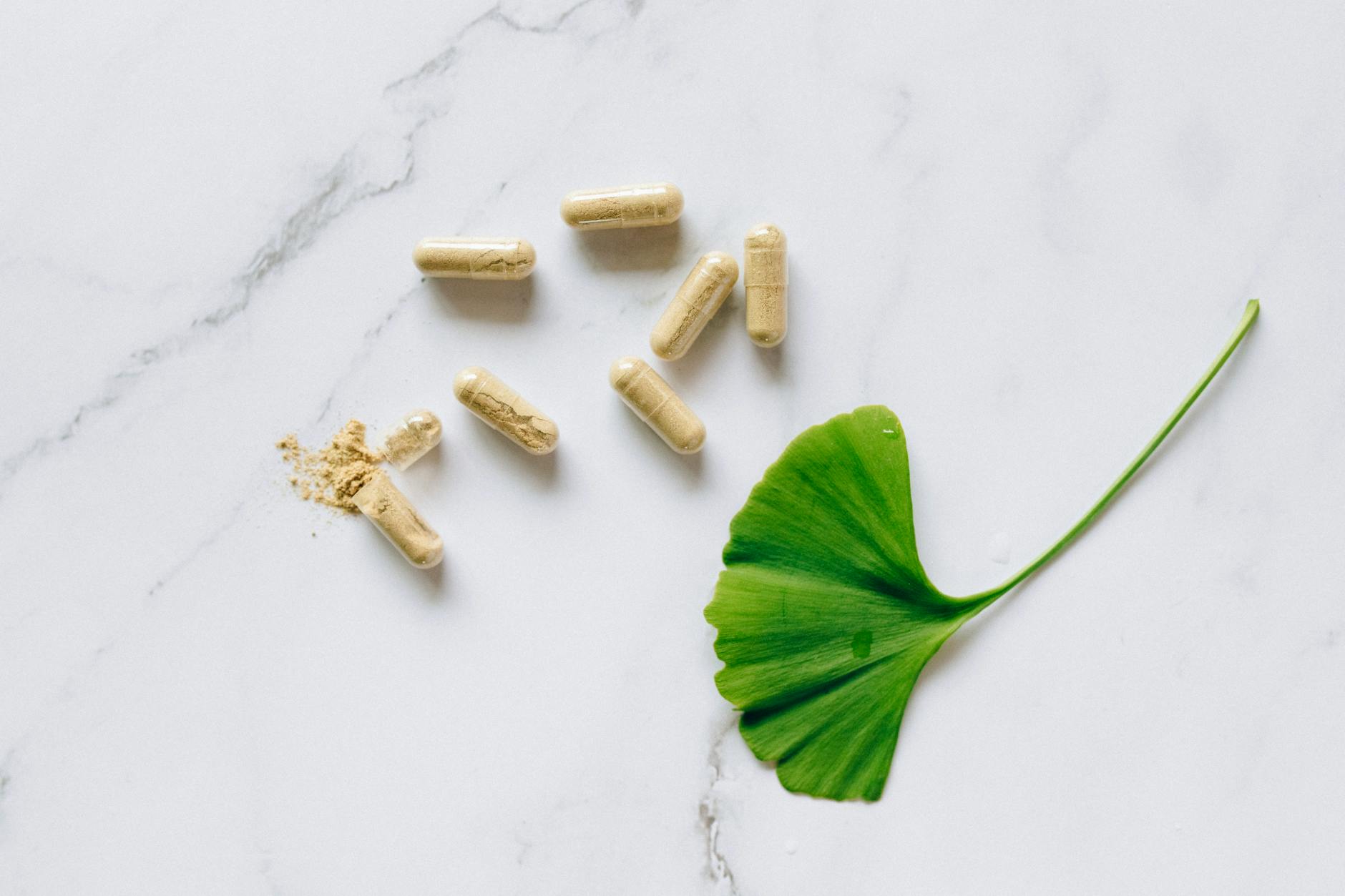 top view of ginkgo biloba capsules with a leaf on a marble surface symbolizing natural supplements