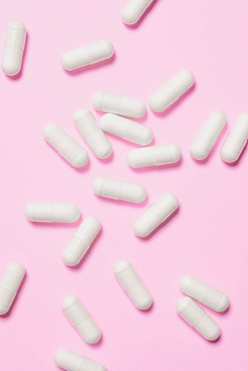 white medicinal capsules scattered on a vibrant pink background symbolizing healthcare and wellness