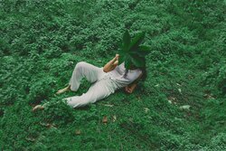A woman relaxing outdoors on lush green foliage, holding a large leaf over her face