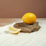 Un citron frais et une tranche sur une surface en bois avec du sable blanc et un fond brun