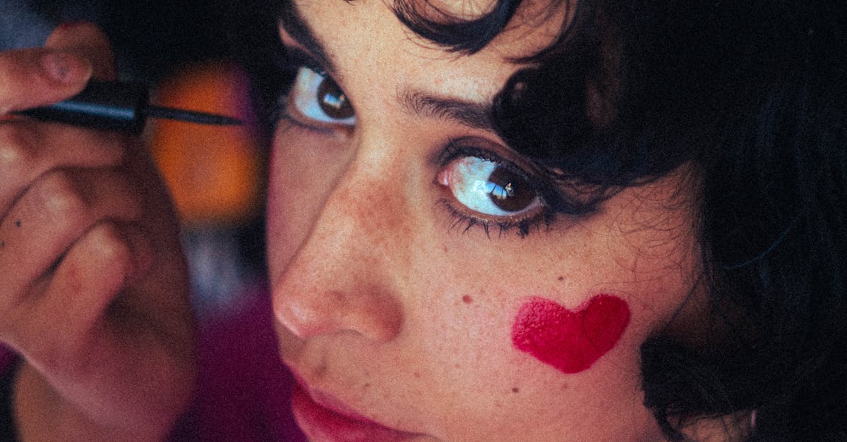 close up of a young woman applying eyeliner with a red heart painted on her cheek