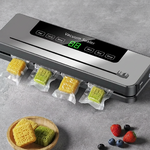 Machine d'emballage sous vide gris argenté sur surface gris béton. Gâteaux de lune jaunes et verts sous vide sortant de la machine. Écran LED vert affichant _88_. Panneau tactile _Vacuum Sealer_ avec boutons Vac,