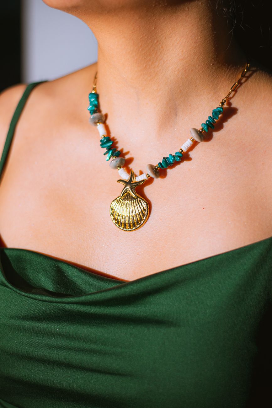 gros plan sur un collier de coquillages orne de pierres turquoise porte par une personne vetue d une robe verte