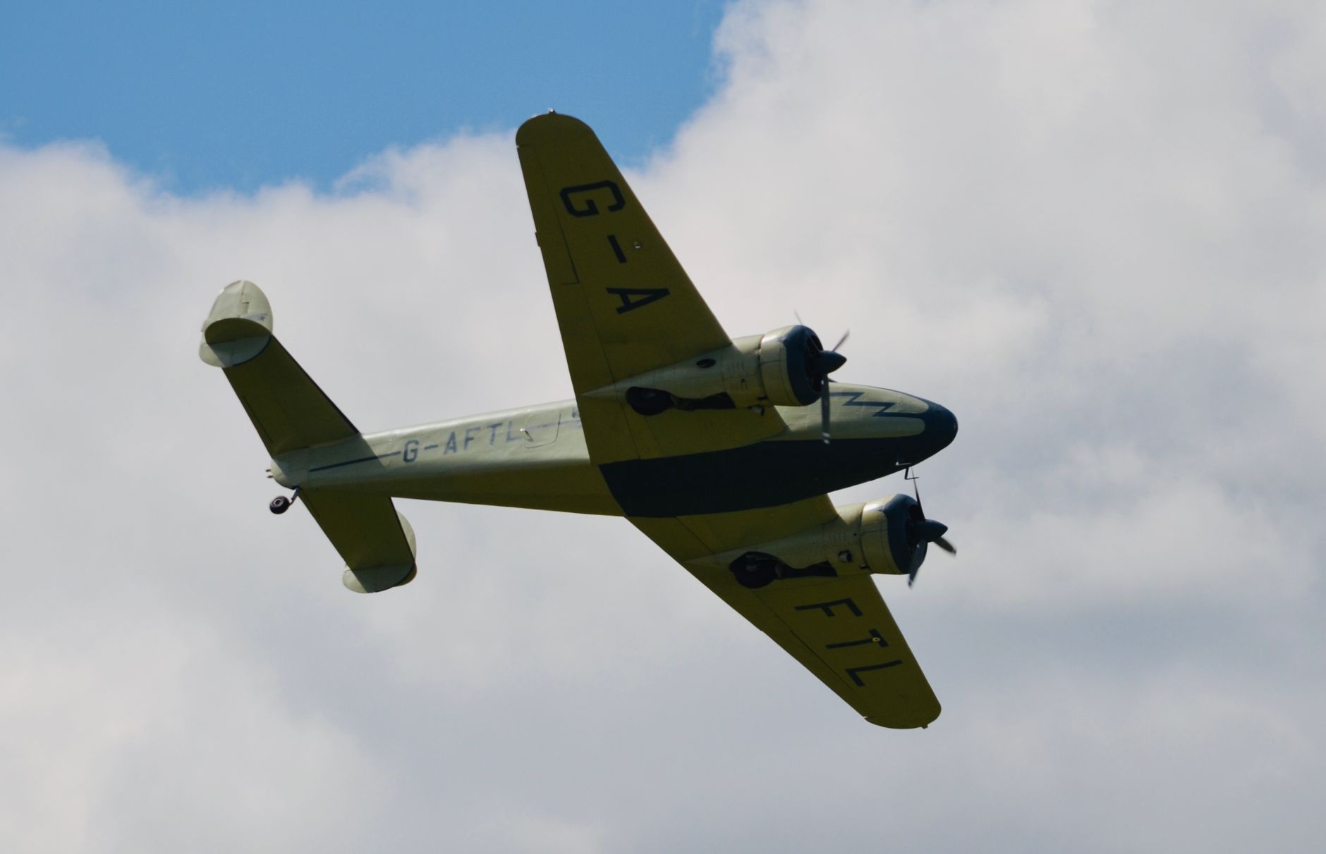 a vintage aircraft with visible markings flying high against a cloudy sky