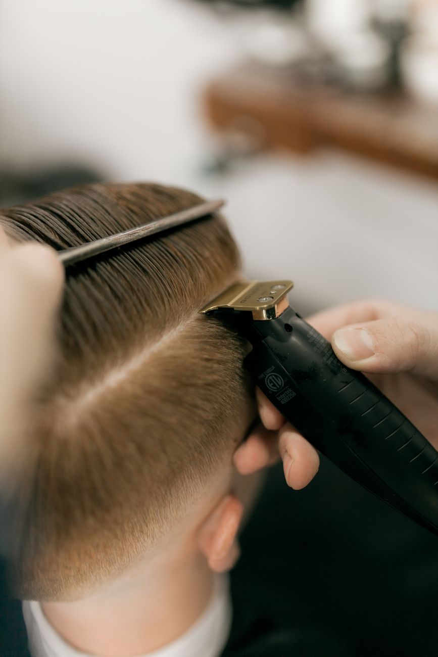 gros plan d un coiffeur utilisant une tondeuse et un peigne pour couper les cheveux d un client dans un salon