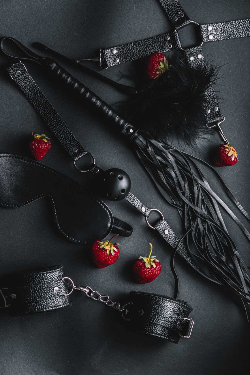 accessoires bdsm en cuir noir avec des fraises sur un fond sombre composition captivante et intrigante