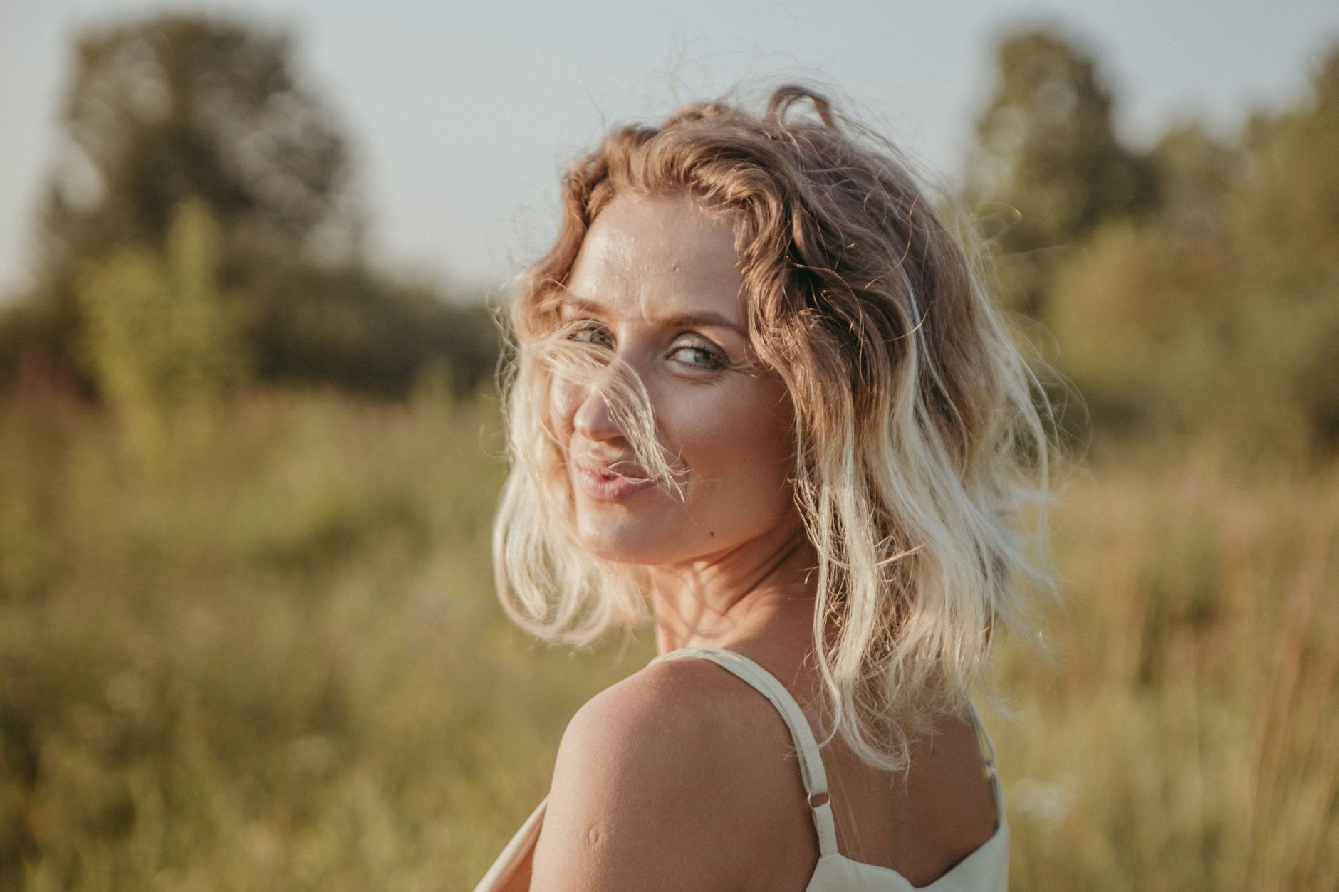 une femme souriante aux cheveux blonds jette un coup d oeil par dessus son epaule dans un champ ensoleille