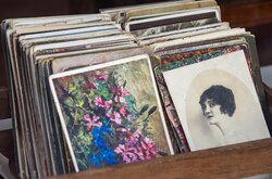Collection de cartes postales anciennes dans une boîte en bois présentant des illustrations florales et un portrait sépia
